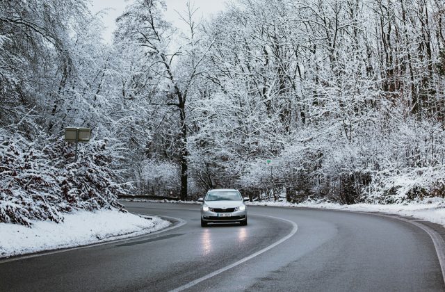 Voiture roulant sur une route de forêt enneigée, phares allumés
