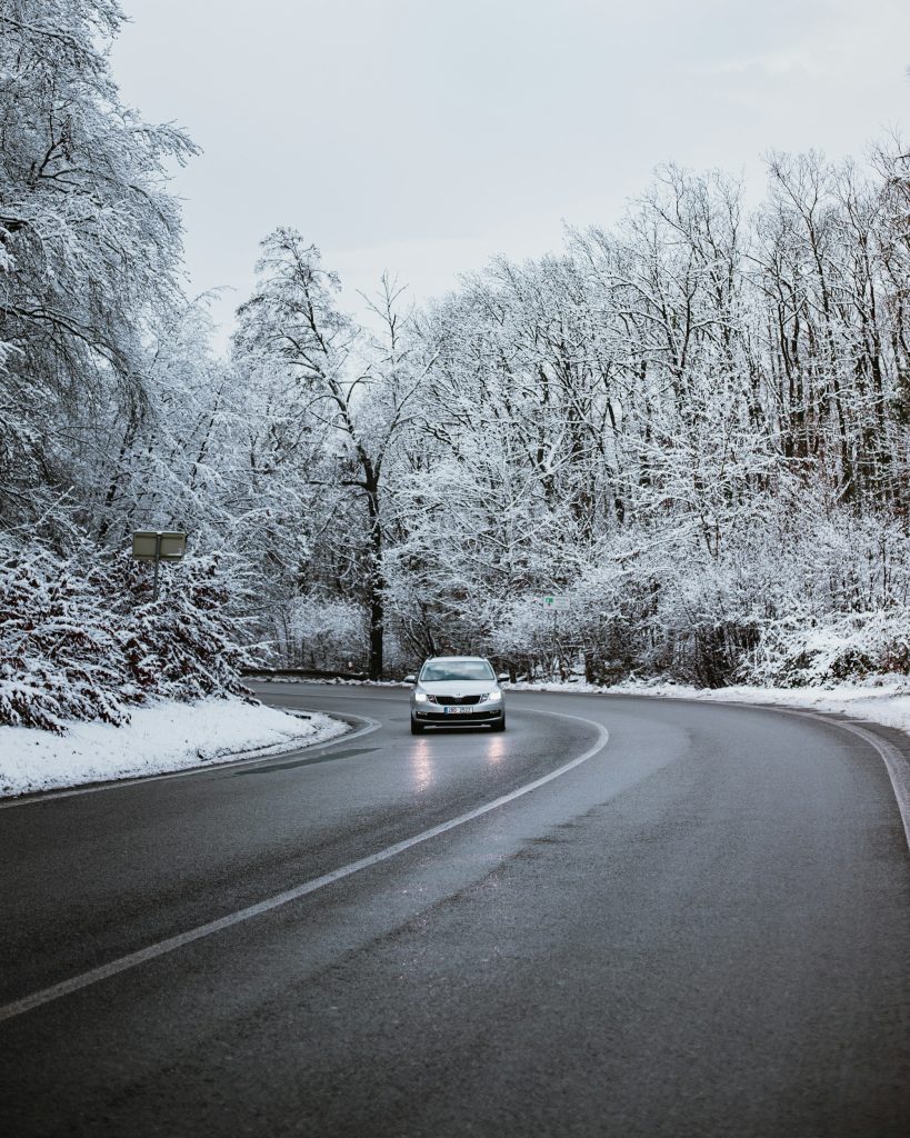 Voiture roulant sur une route de forêt enneigée, phares allumés